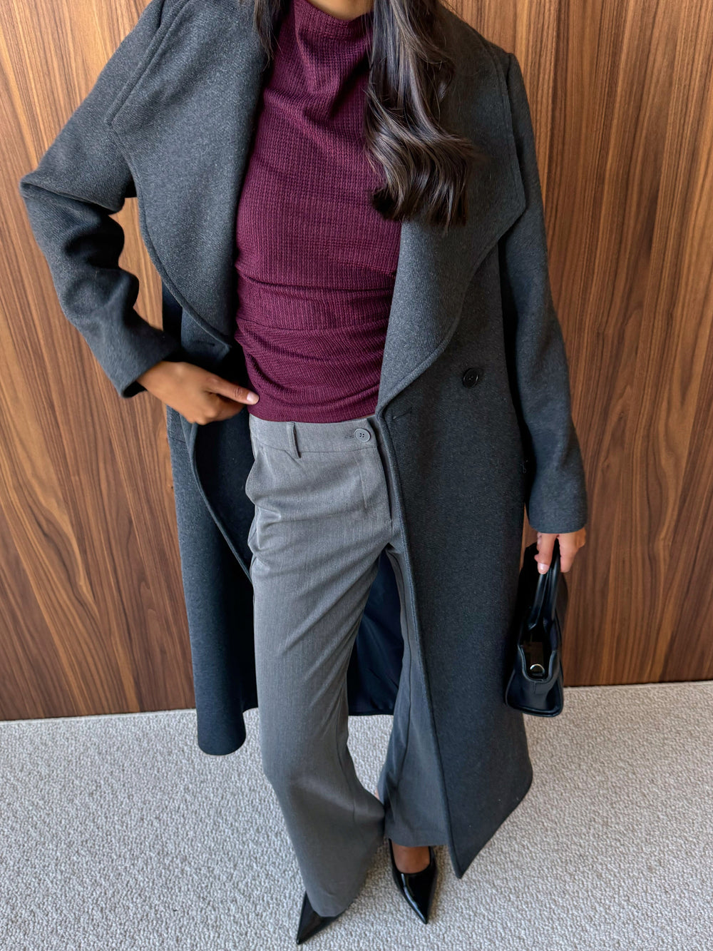 Berry red high-neck top, grey suit trousers and a grey coat.